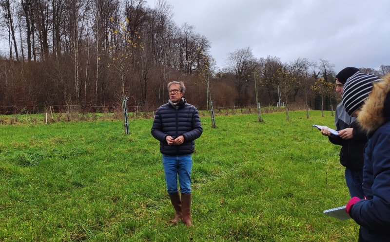 M Heins arboriculteur est dans une de ses vergers, il explique aux étudiants en présence des enseignats qui les accompagnent comment on plante, entretien, récolte les fruits : ici essentiellement des pommiers de variétés locales.